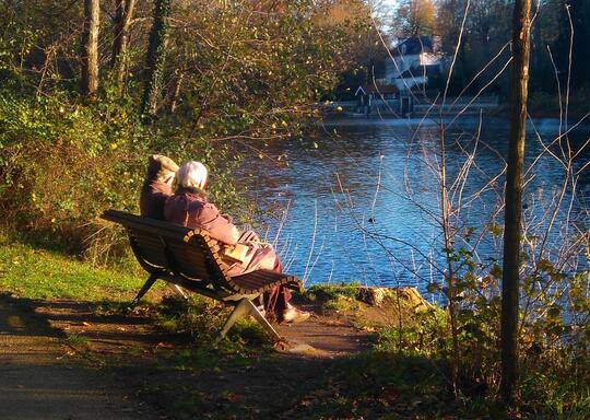 Illustrasjonsfoto med et eldre par på en benk ved vannet. Adobe Stock foto.